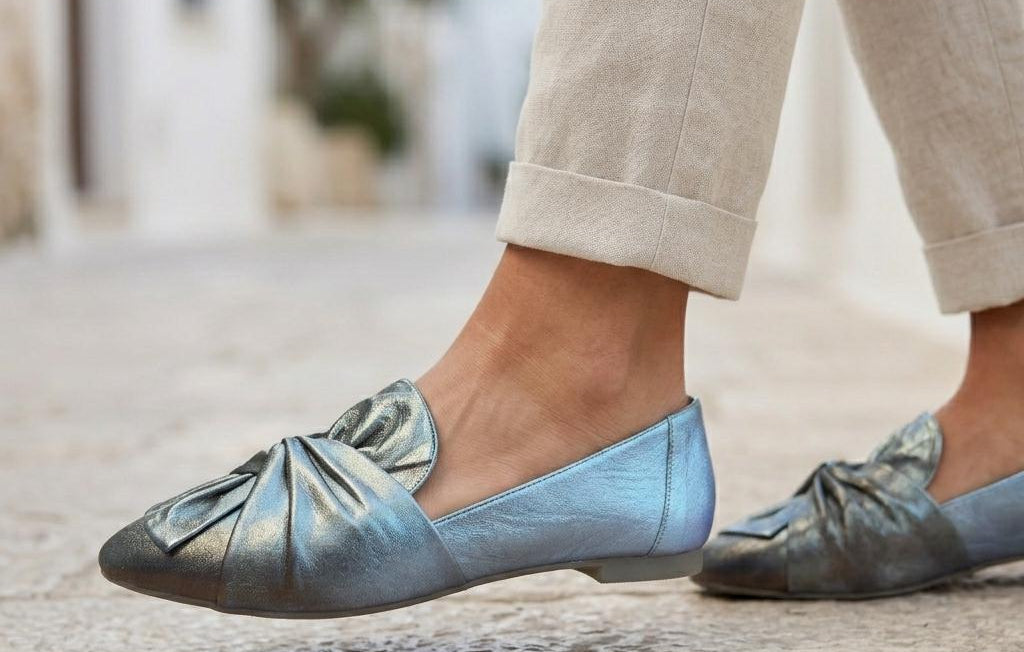 Light blue flats worn with beige pants on a blurred outdoor background